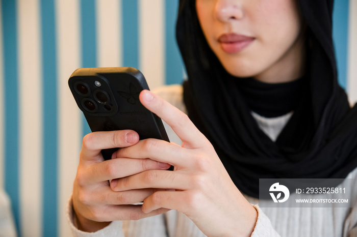 Young woman in hijab using phone in cafe