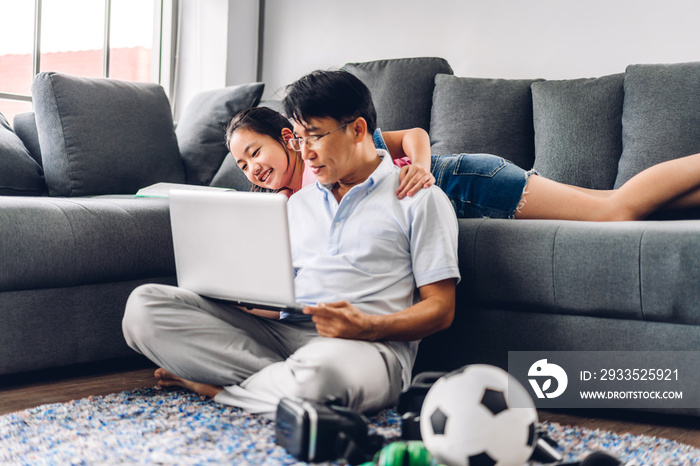 Smiling asian man relaxing using laptop computer working and video conference meeting chat with his girl daughter learning reading book and studying knowledge at home.work from home concept