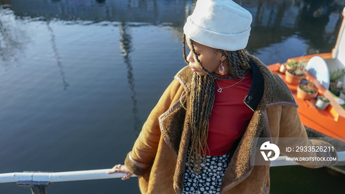 Young woman with braided hair and cap leaning on railing by river