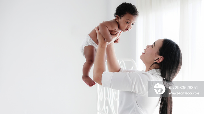 portrait of asian mother and her black mixed race baby girl in white room