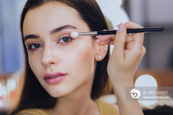 Pink lips. Green-eyed good-looking woman with pink lips using eye shadows while putting makeup on