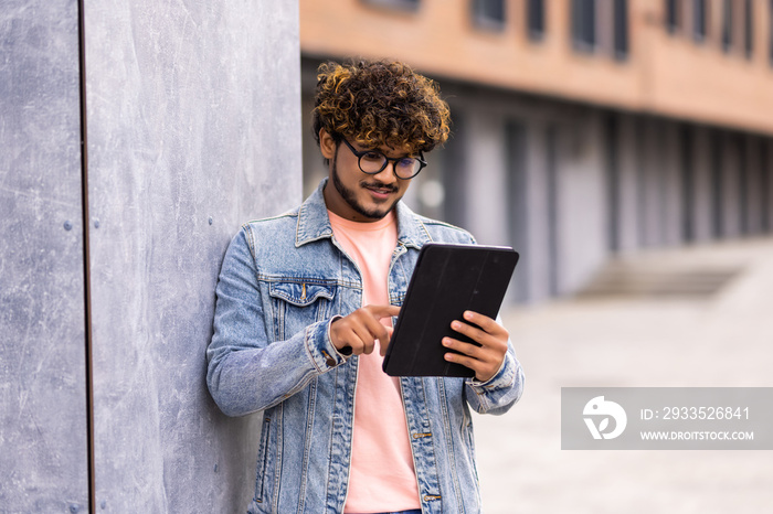 Young indian male using tablet outdoor on the street