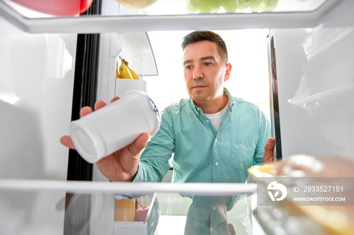 food, eating and diet concept - middle-aged man taking yoghurt from fridge at kitchen