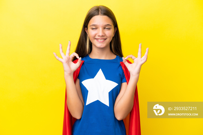 Little caucasian superhero girl isolated on yellow background in zen pose