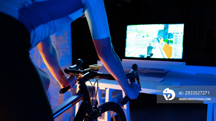 Asian man cycling on the machine trainer he is exercising in the home at night.he play online bike game