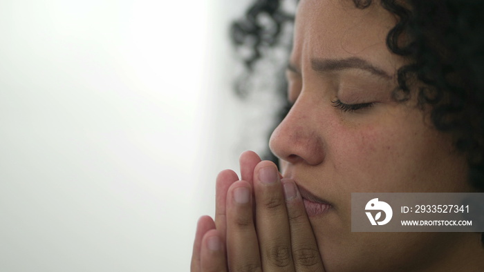 One spiritual young black woman face in prayer. Meditative contemplative Brazilian adult girl praying. Person having HOPE