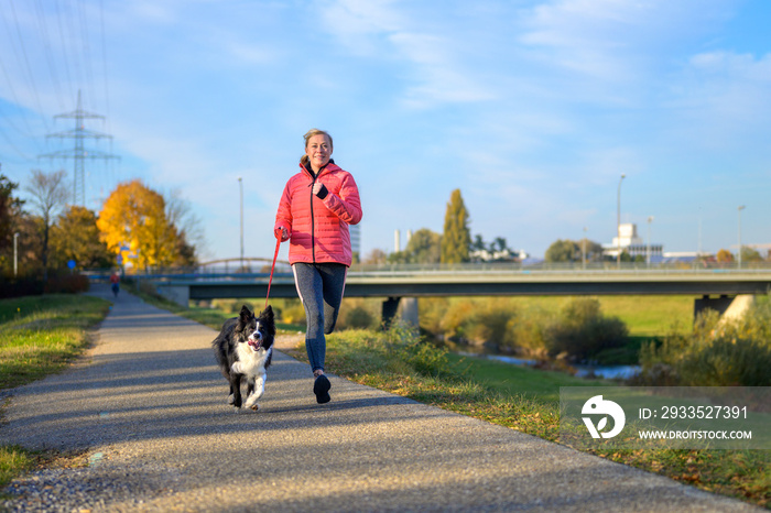 Fit athletic woman running with her Border Collie along footpath