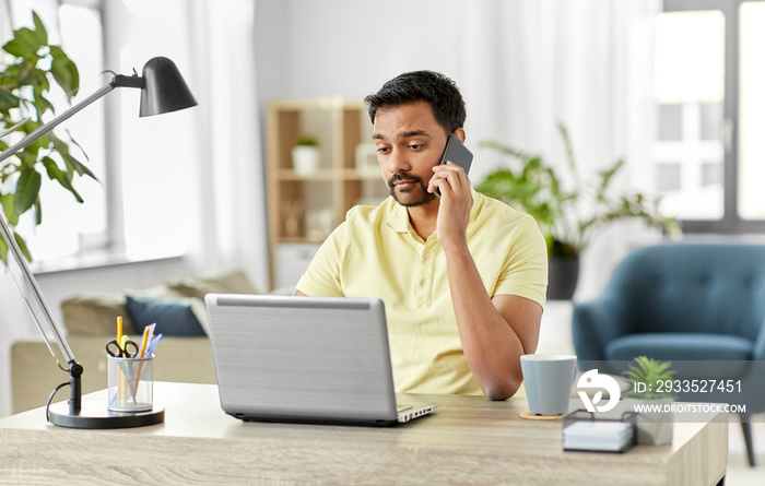 technology, communication and remote job concept - indian man calling on smartphone with laptop computer working at home office