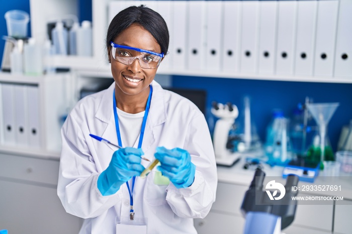 Young african american woman scientist smiling confident writing on test tube at laboratory