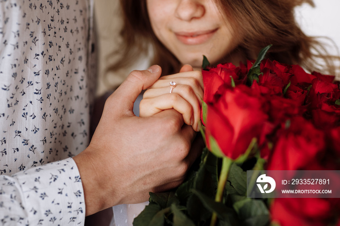 young man holding his fiance’s hand with gold ring while making a marriage proposal with bouquet of red roses. Engagement of a young couple in love. The concept of love and togetherness.