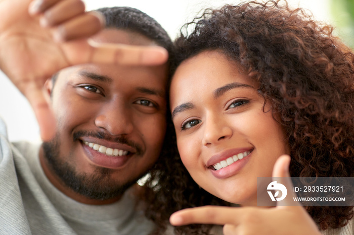 people concept - happy african american couple making selfie or viewfinder viewfinder gesture at home