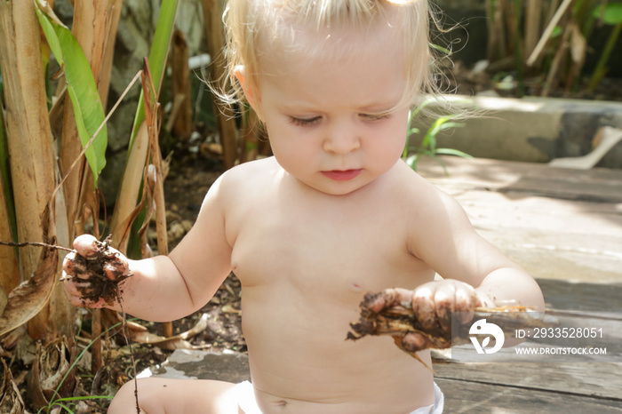 Portrait of adorable blonde baby playing in the garden. Letting your baby get dirty is how baby explores the world and one of the best places to learn that is in the garden.