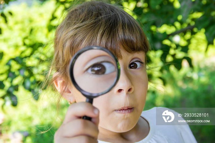 The child is looking in a magnifying glass. Increase. selective focus.