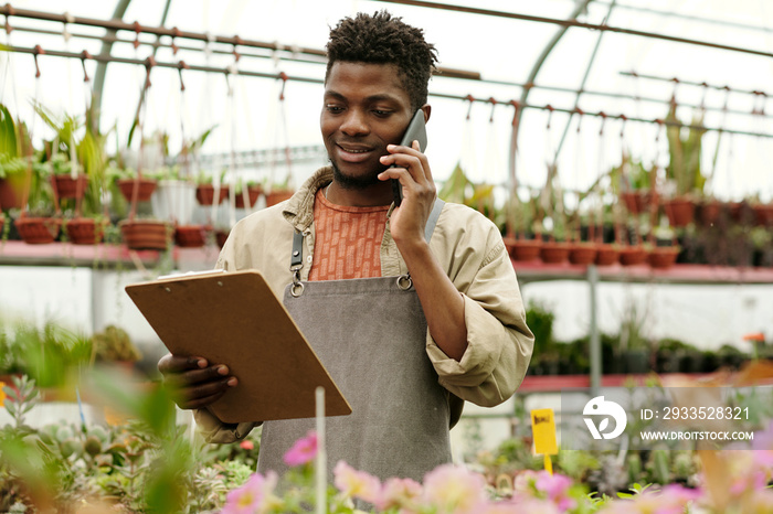 Flower shop owner looking at document in his hands and taking an order from customer by mobile phone