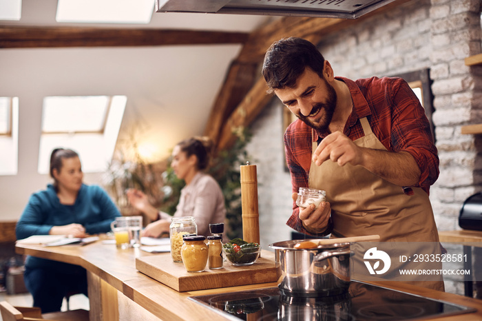 Happy man adding salt while cooking for his friends in the kitchen.