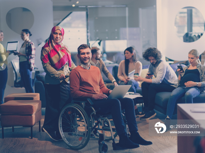 Disabled businessman in a wheelchair at work in modern open space coworking office with team