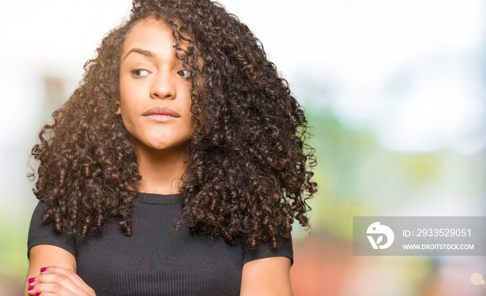 Young beautiful woman with curly hair smiling looking side and staring away thinking.