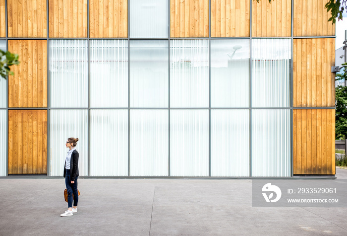 Young businesswoman walking outdoors with bag on the office wall background. Wide shot with copy space