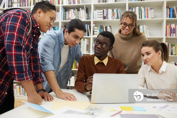 Multi-ethnic group of students studying together in college library, focus on African-American man using laptop, copy space