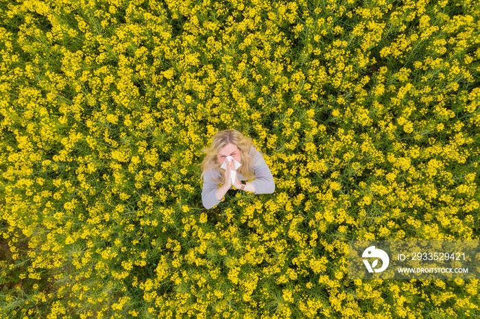 Young woman suffers from allergy in a rape field and has to sneeze