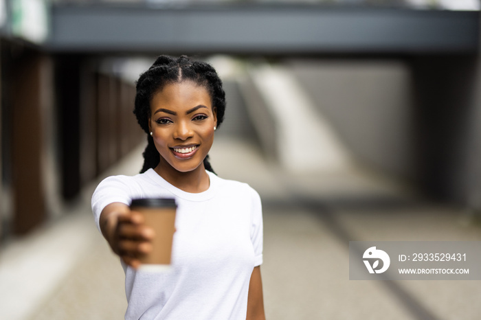 Cheerful young african woman walking outdoors, holding takeaway coffee cup and pointed on you