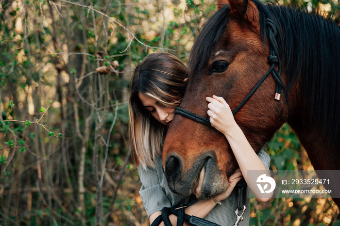 Beautiful young woman hugging brown horse and wearing dress