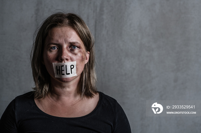 Beaten up woman victim of domestic violence and abusewith covered her mouth taped with the inscription  help . Empty space for text