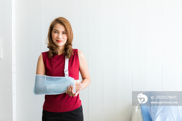 Portrait of asian female patient in red dress broken arm after accident and wear arm splint for treatment and bed in the room hospital background,copy space