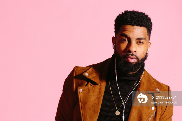 Cool young African American man with beard looking at camera, isolated on pink studio background