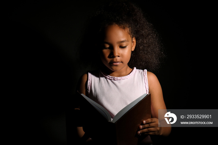 Little African-American girl reading book on dark background