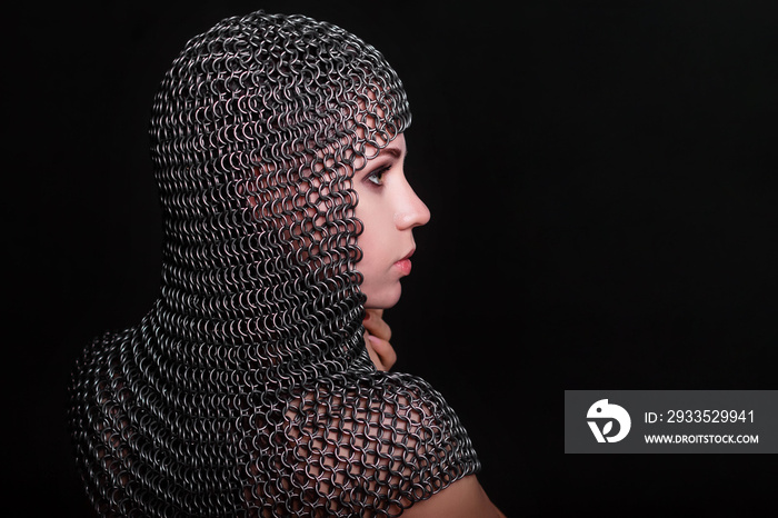 Portrait of a beautiful, young girl in a chainmail hood on a black background. Model with clean skin.