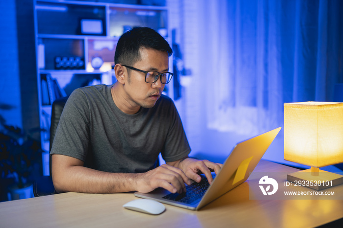 freelance man working on laptop At home at night. Man freelancing, thinking, serious while working at home at night. Freelance work and work from home concept.