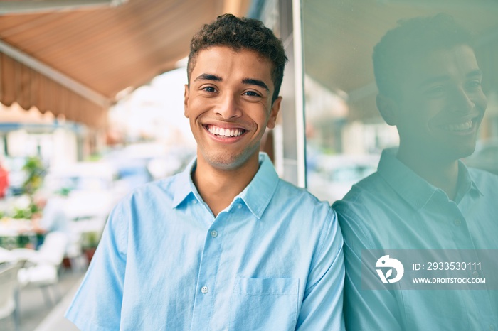 Young latin man smiling happy leaning on the wall at the city.