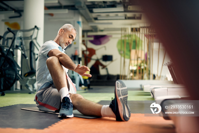 Mature athletic man stretching on the floor while exercising in a gym.