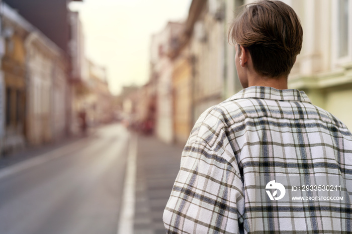 Rear view short hair woman in plaid shirt walking down street in town.