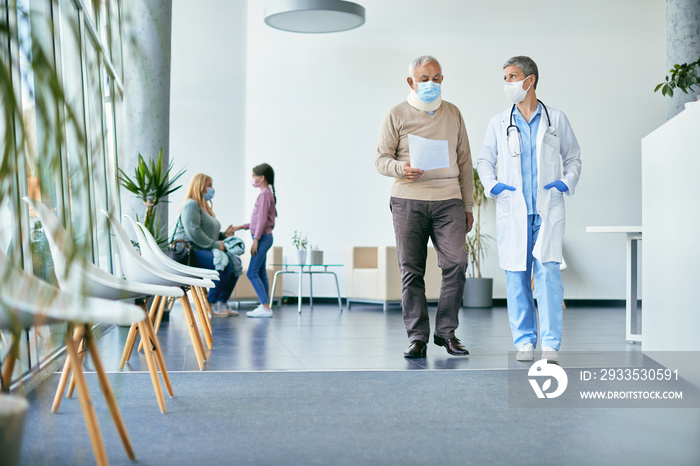 Senior patient with neck collar and his doctor analyzing medical report while walking through hallway at the hospital.