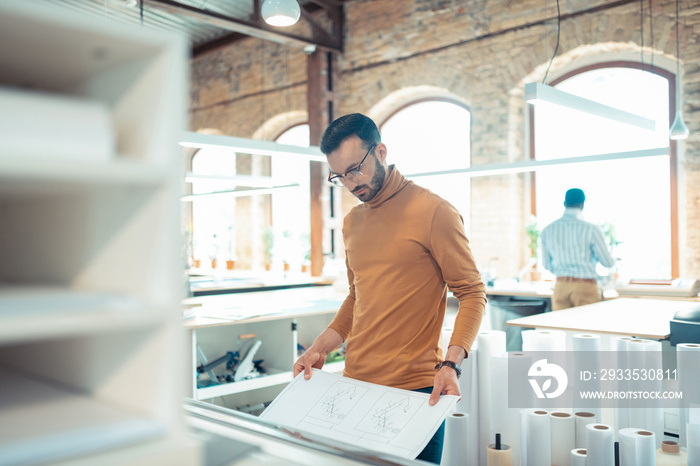 Dark-haired man wearing glasses standing near big printer