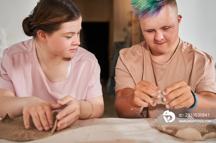 Teens with down syndrome looking at the each other while making dishes from clay