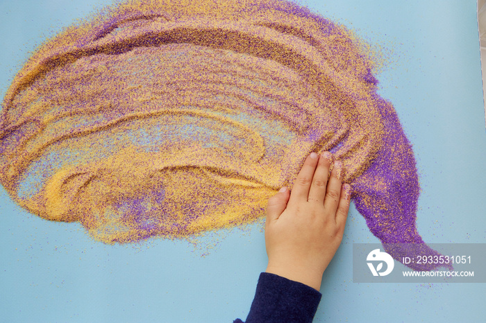 Baby hands play with colorful sand. Creative place for product. Child fine motor skills development. Creative kids occupation. View from above. Copy space.