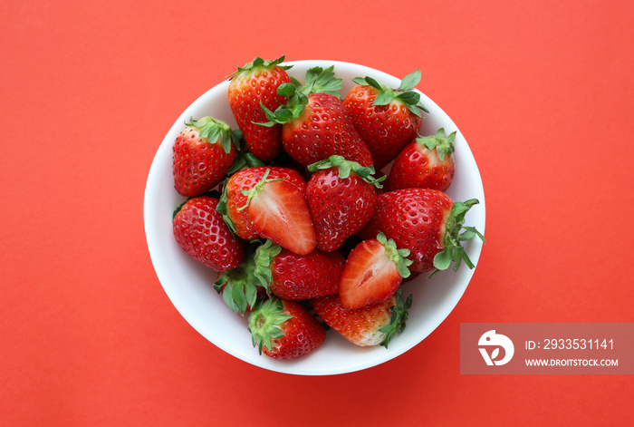 Fresh and ripe strawberries in a white bowl on red background. Top view. Concept of healthy food.