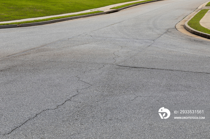 Street leading into an intersection, weathered and cracked asphalt street surface, horizontal aspect