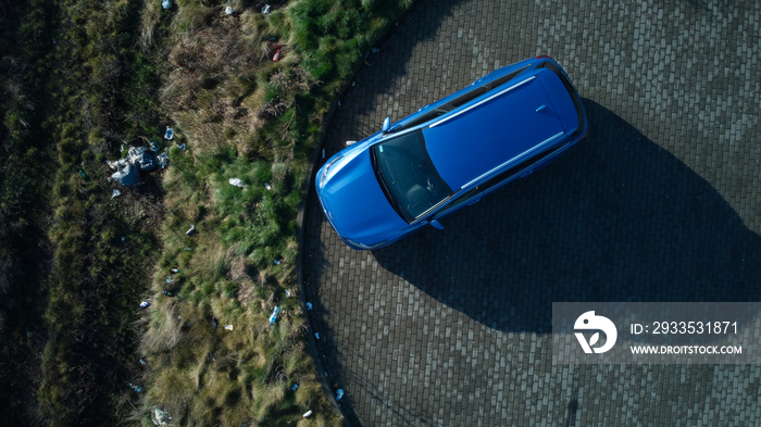 A blue car standing in a cobblestone parking place. Garbage thrown nearby. Aerial drone, top down view.