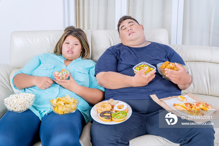 Fat couple sleeping while eating and watching tv