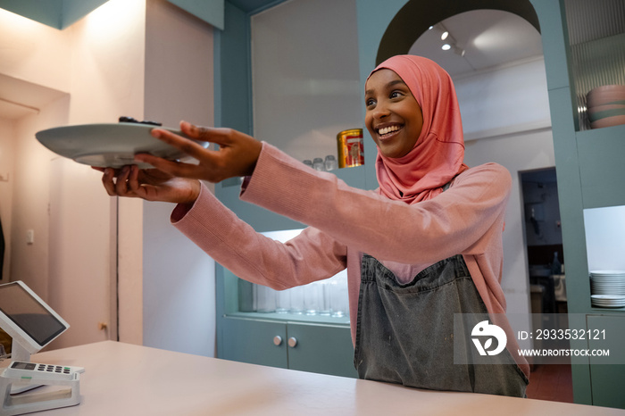 Smiling young woman in hijab working in cafe