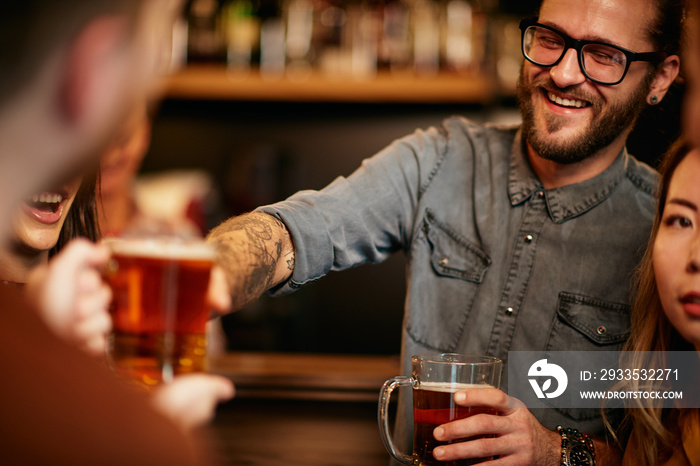 Group of friends drinking beer, chatting and having good time at pub. Night out.