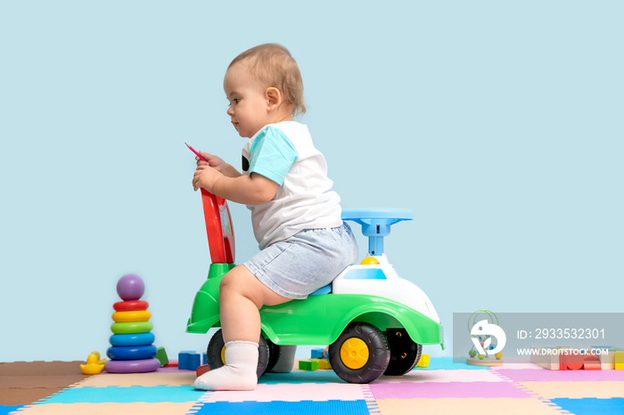 Toddler 15-20 months sitting on a children’s toy car backwards in the playroom.