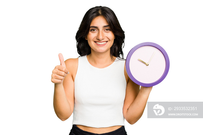 Young Indian woman holding a clock isolated smiling and raising thumb up