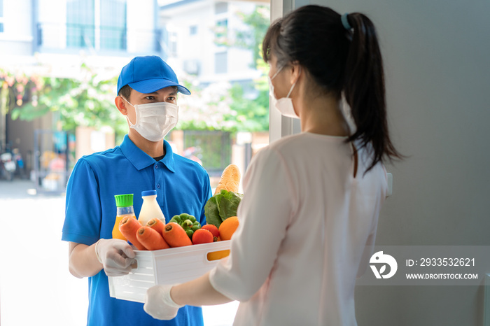 Asian woman costumer wearing face mask and glove receive groceries box of food, fruit, vegetable and drink from delivery man   in front of the house during time of home isolation.