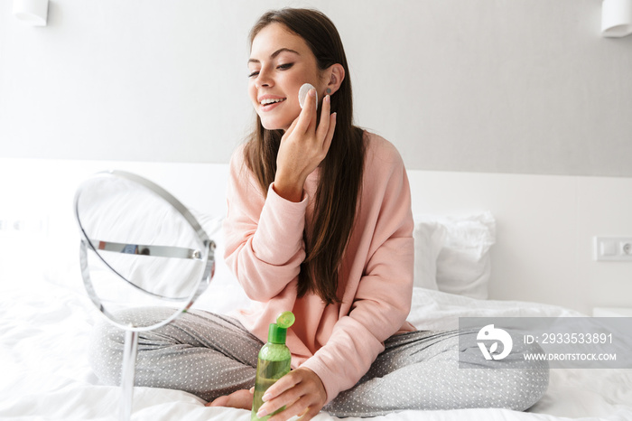 Smiling lovely girl wearing pajamas applying tonic