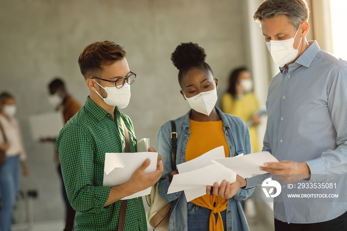 University professor and two students wearing face masks while communicating in a hallway.